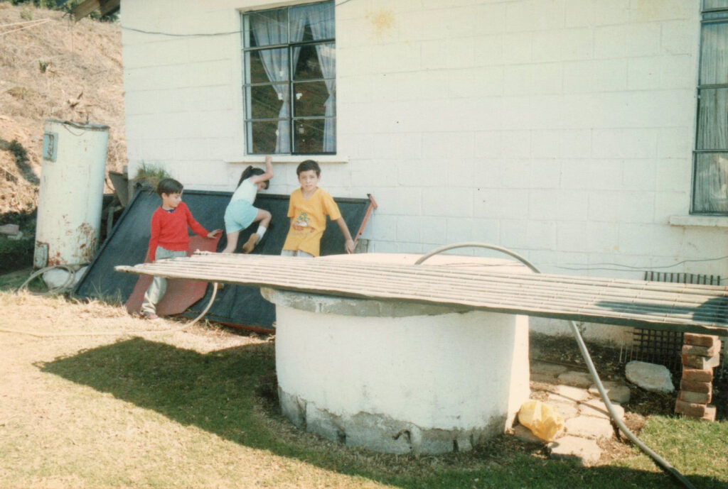 Max Lainfiesta (on right) and his siblings, playing around a prototype unglazed serpentine solar water collector, 1986.
