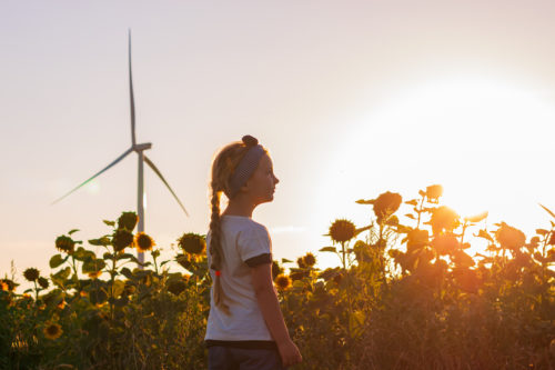 girl in front of sunflower field and wind turbine