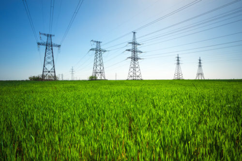 High voltage lines and power pylons in a green agricultural landscape with blue sky on a sunny day.