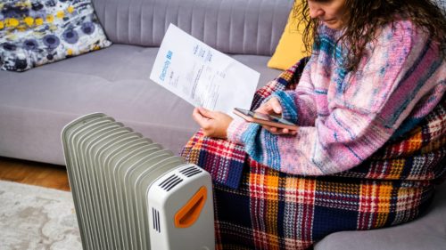 woman sitting by a heater paying energy bill