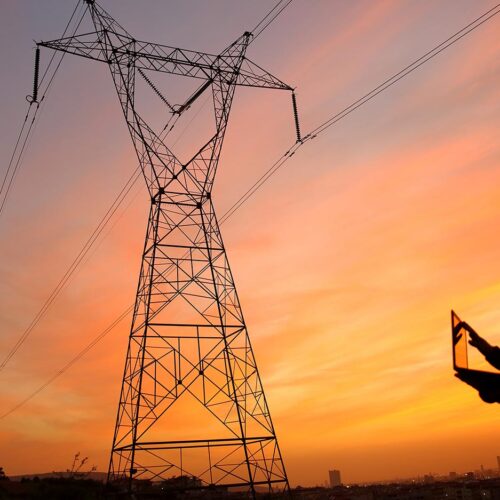 man with laptop at powerlines at sunset