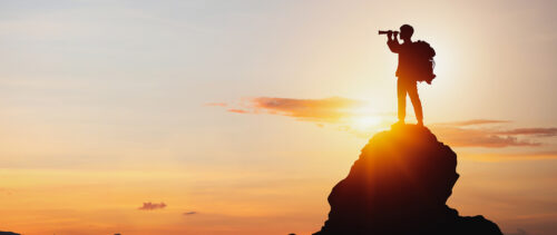 silhouette of a man using spyglass on mountaintop