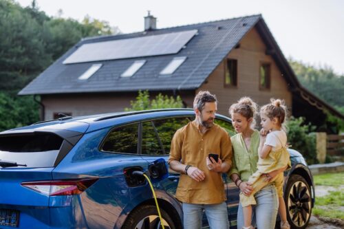 a family stands in front of their EV and house